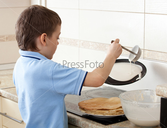 Child bakes pancakes in the kitchen. Boy cooking breakfast