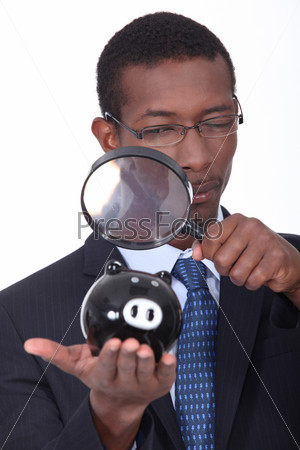 black well dressed man watching a piggy bank with a magnifying glass