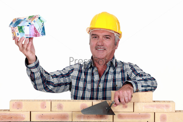 Tradesman holding up a house model make out of money