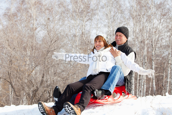 Mature couple sledding. Seniors couple on sled in winter park