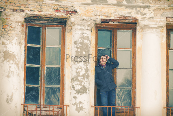 The man in warm jacket posing near an old house in winter