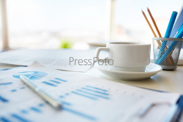 Close-up image of an office desk at morning with a cup of tea and financial documents