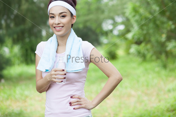 Sportswoman wearing a headband smiling at the camera holding a small bottle of water