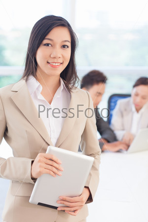Vertical shot of a smiling smartly dressed business girl holding a digital pad