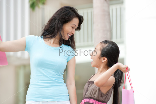 Smiling mother and daughter looking at each other and holding bags after shopping