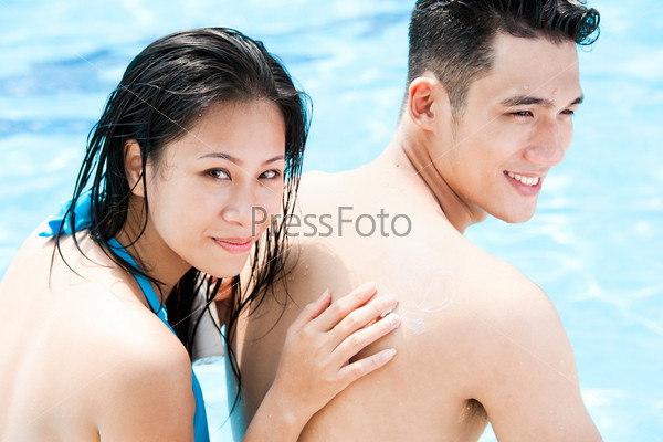 Smiling woman applying suntan lotion on her boyfriendÃ¢Â?Â?s shoulder