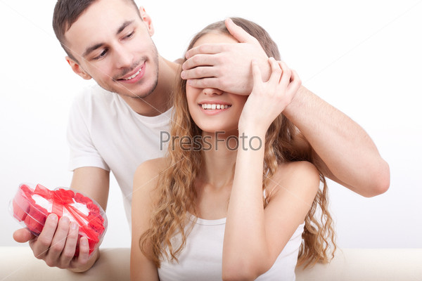 Young man gives his girlfriend a heart-shaped box, he covered her eyes with hand, stock photo