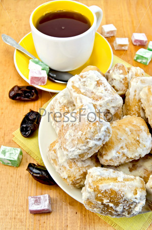 Baursak on a plate, a cup of tea with a spoon, of different color lokum and figs on the background of wooden boards