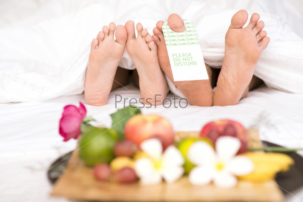 Image of two pairs of bare feet of man and woman lying under blanket with low calorie breakfast in front