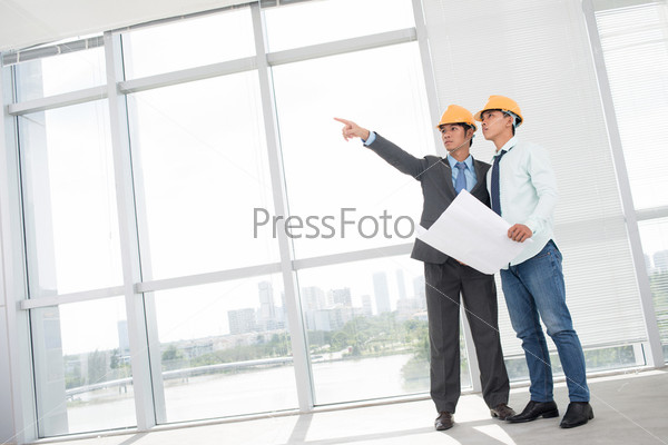 Tilted image of two supervisors comparing blueprint with actual building interior