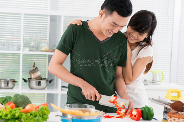 Smiling couple spending time together in the kitchen, guy chopping vegetables