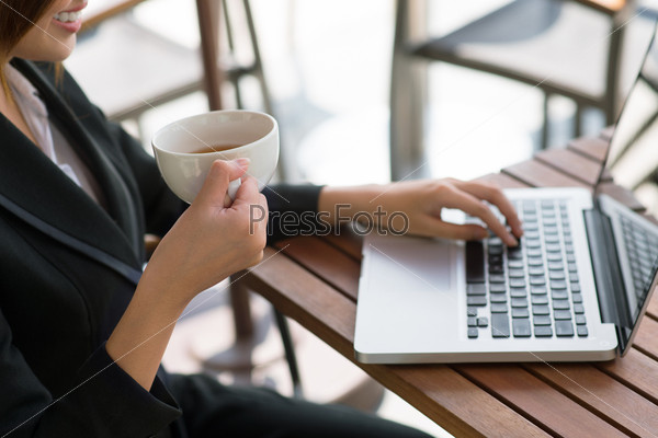 Positive business lady using her laptop and drinking tea