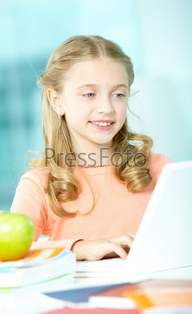 Portrait of smart schoolgirl sitting in classroom and typing