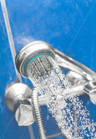 A shower head is spraying water on the blue background in bath room. Spa health concept