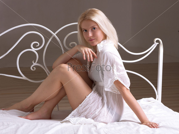 Blonde girl in the bed next to wrought headrest, stock photo