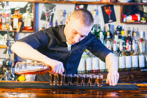 Young professional barman in action making  drink shots