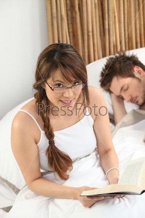 Woman reading a book beside a sleeping man