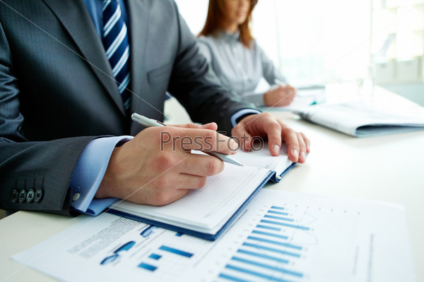 Image of male hand with pen over page of notebook at seminar, stock photo