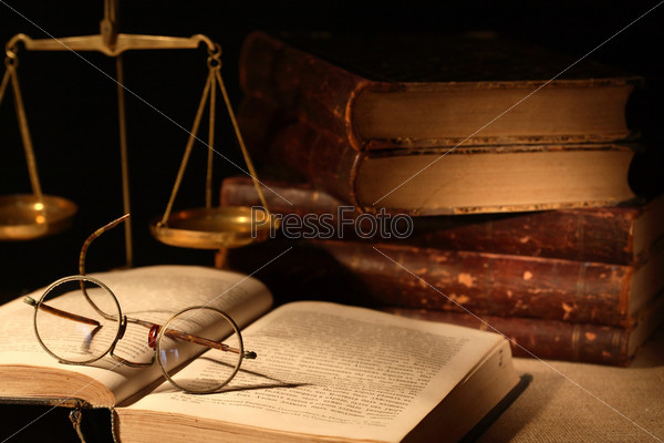 Vintage still life with spectacles on open book near brass weight scale on dark background