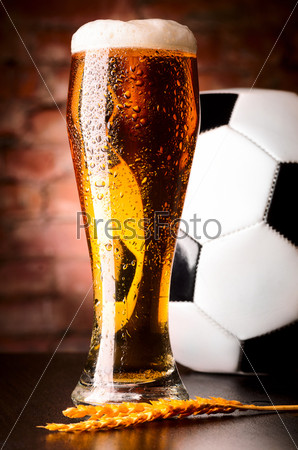 glass of lager on table with soccer ball against brick wall