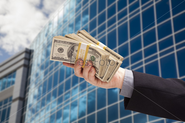 Male Hand Holding Stack of Cash with Corporate Building Background.