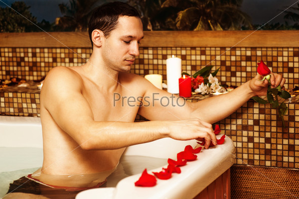 Young man in spa. Romantic jacuzzi with flowers and candles. man decorated bathroom with rose petals waiting for his beloved. Preparing for a date