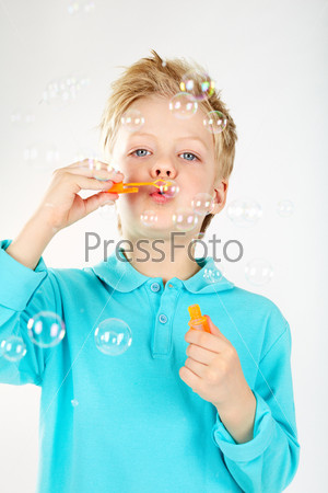 Cute boy blowing soap bubbles and looking at camera