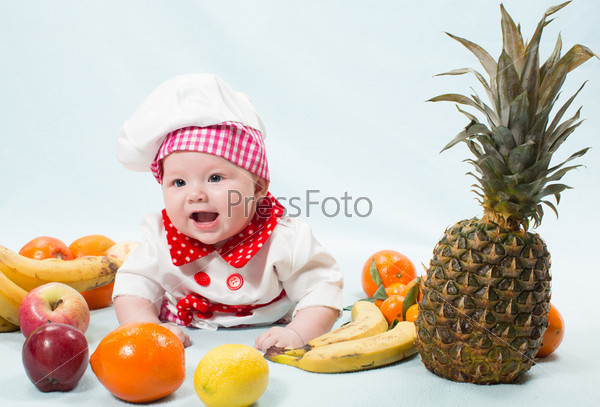 Portrait of smiling baby wearing a chef hat surrounded by fruits. Use it for a child, healthy food concept
