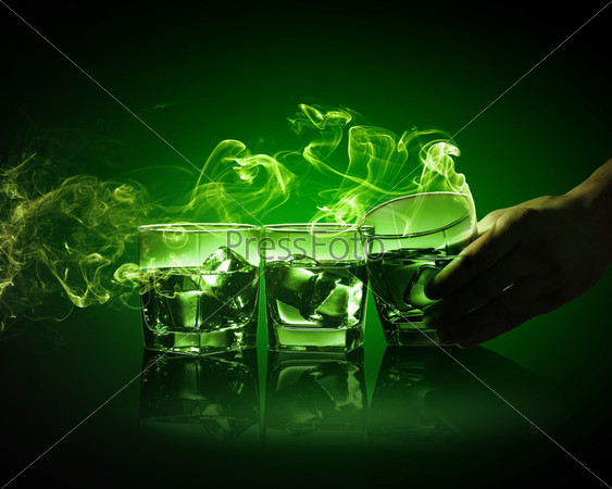 Hand holding one of three glasses of green absinth with fume going out