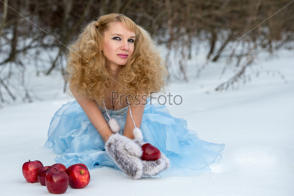 Appealing young Snow Maiden (the granddaughter of Father Frost) in a transparent blue dress poses at winter forest with apples