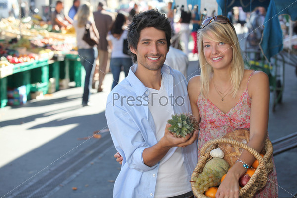 Молодая пара с корзиной фруктов на людном рынке