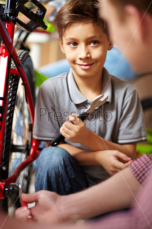 Portrait of cute boy looking at his father while repairing bicycle in garage