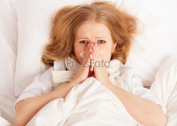 Ill sick young woman sneezes into a handkerchief in bed