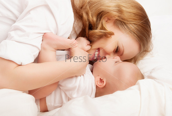 happy family. baby and mother play, kiss, tickle, laugh in white bed
