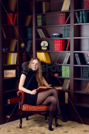 Clever young woman sits on couch and reads book at home.