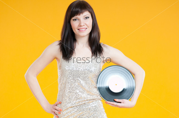 Smiling young woman posing with a vinyl disc, yellow background