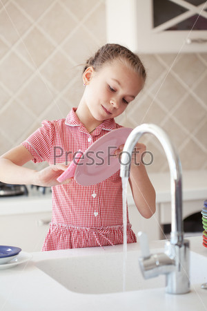 Portrait of a 6 years old girl washing the dishes at home