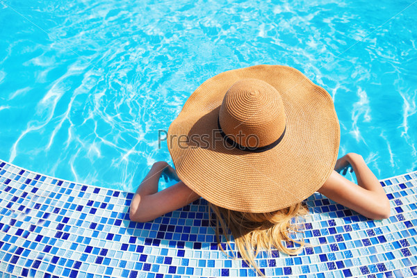 Pretty woman in a hat enjoying a swimming pool