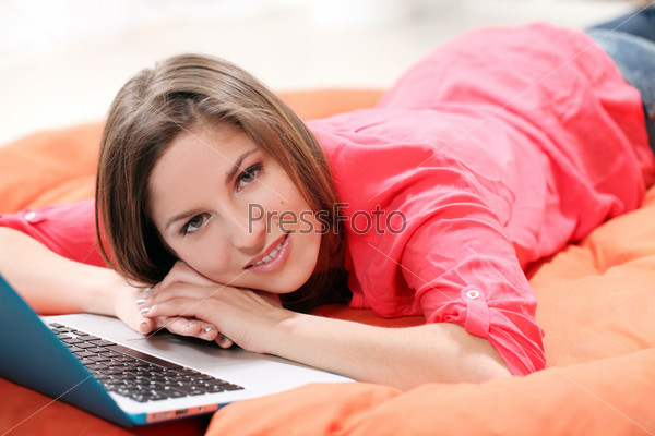 Happy young woman with laptop lying on an orange blanket