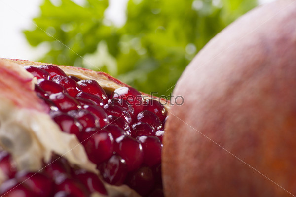 pomegranate cut by peaces close-up on white background with green leafs, horizontal orientation