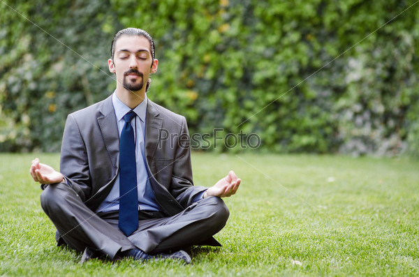 Young businessman meditating in the garden, stock photo