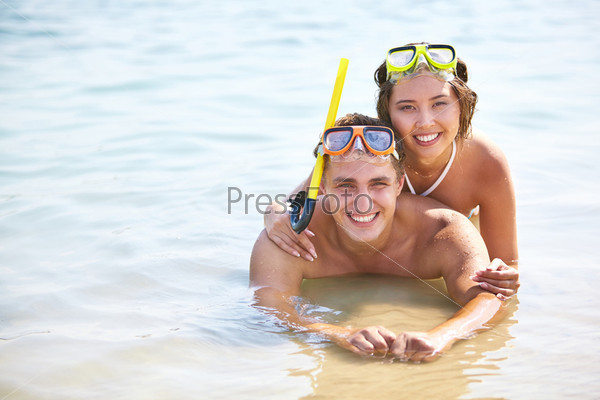 Copy-spaced portrait of smiling young people in scuba masks lying in water