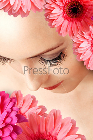 Female beautiful face with false extralong eye lashes close up and gerbera flowers