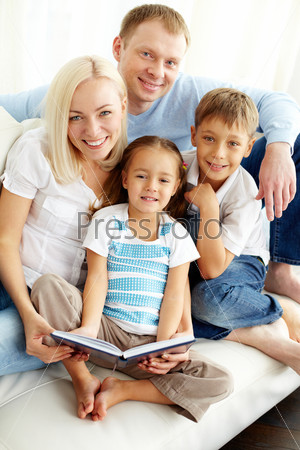 Portrait of happy family looking at camera while reading book