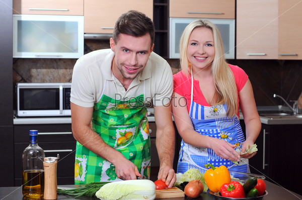 Young couple cooking - man and woman in their kitchen at home preparing vegetables for salad