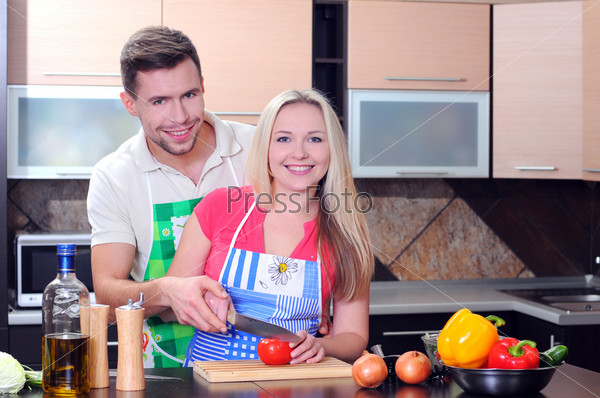 Young couple cooking - man and woman in their kitchen at home preparing vegetables for salad