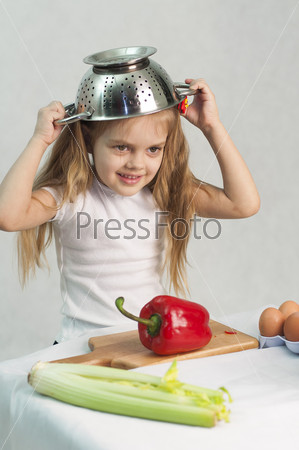Girl playing in a cook. Carried away by the game she put on a colander on his head. Studio. Light background.