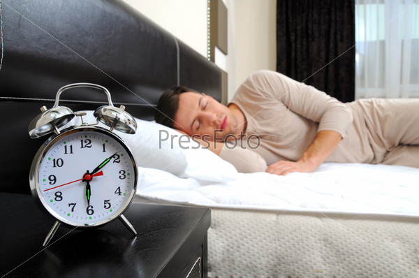 A man is sleeping with an alarm clock in front