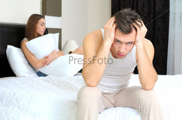 Upset man having problem sitting on the bed with his girlfriend