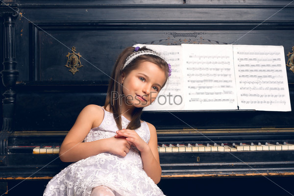 Счастливая девочка в красивом платье сидит за фортепиано